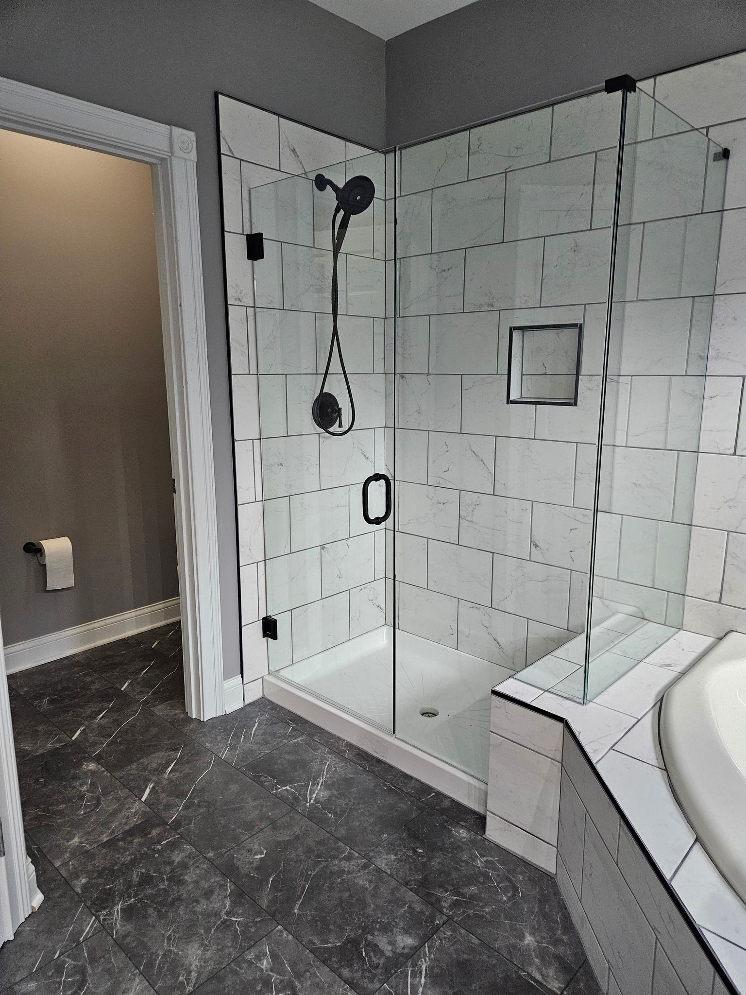 Modern bathroom with glass shower, white tile walls, black fixtures, and gray floors.