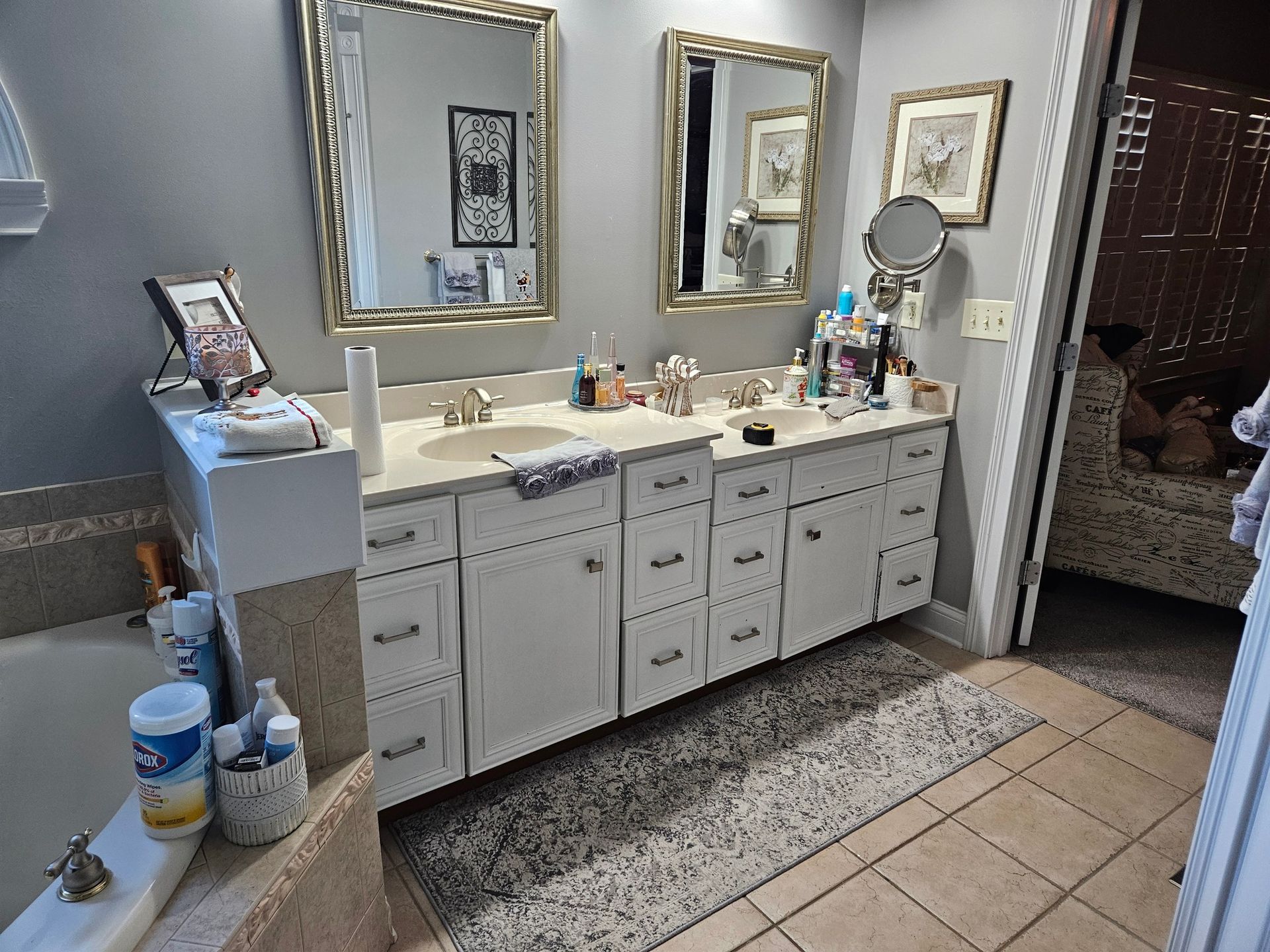 A bathroom with two sinks, mirrors, and a vanity. White cabinets, gray walls, and tan tile floor.