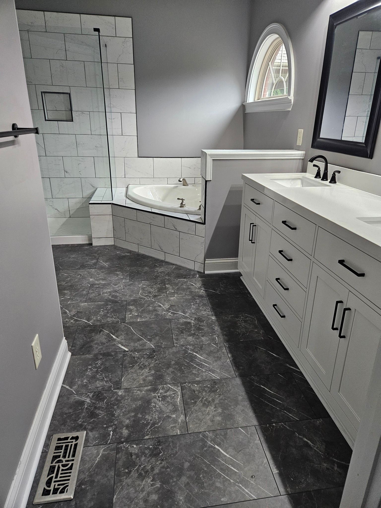 Gray bathroom with tiled floor, white vanity, shower, and arched window.