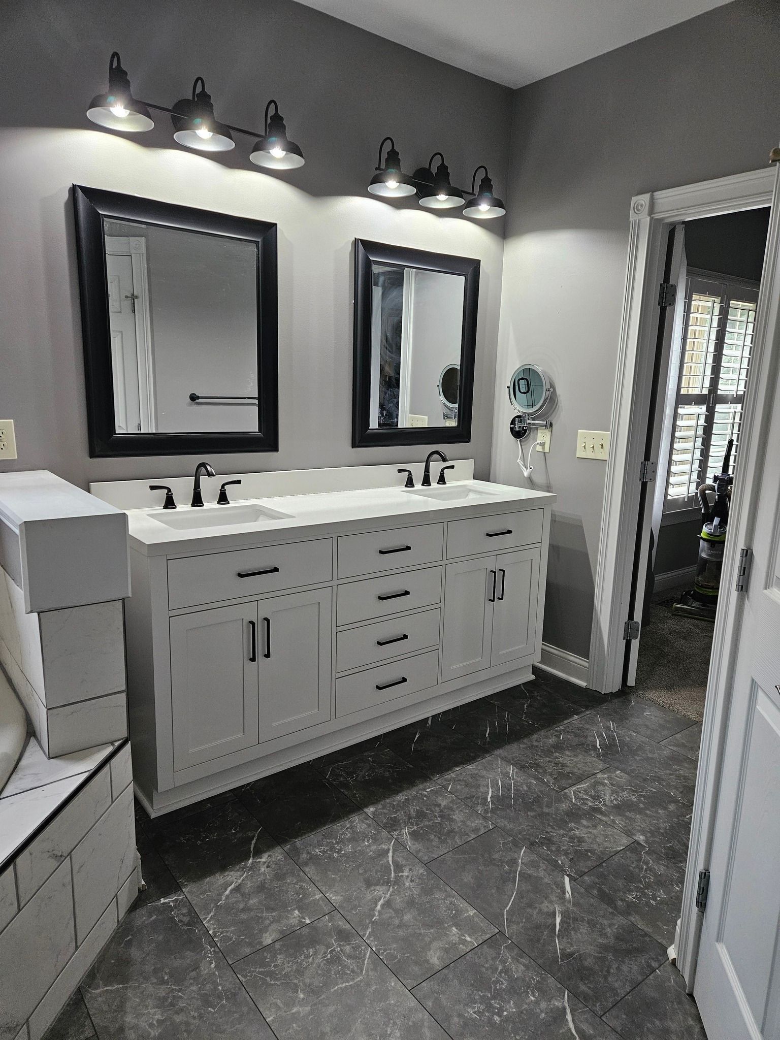 Bathroom with white double vanity, black framed mirrors, gray walls, and dark tiled floor.