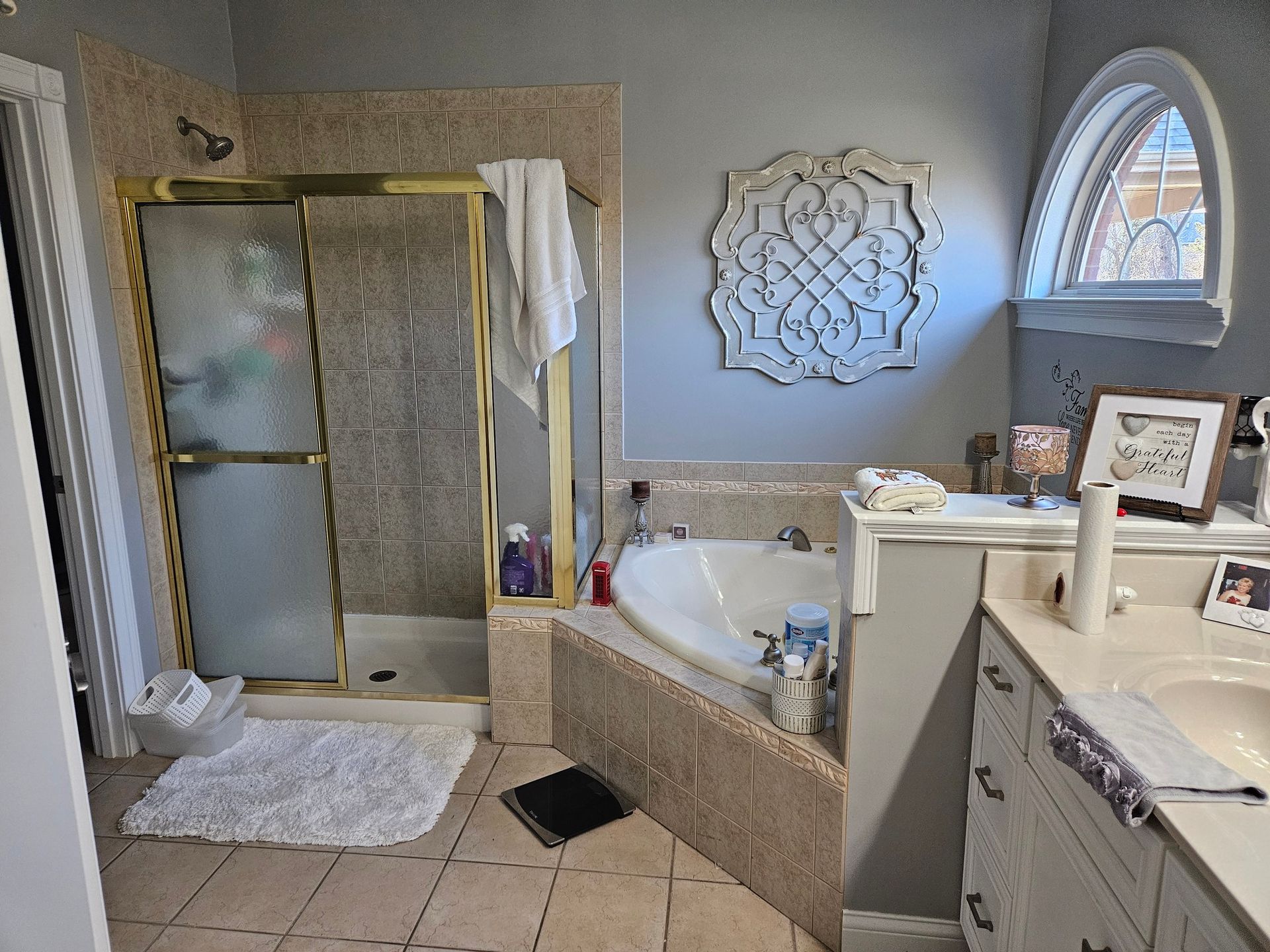Bathroom with shower, tub, sink, and decorative mirror. Light-colored tile and walls.