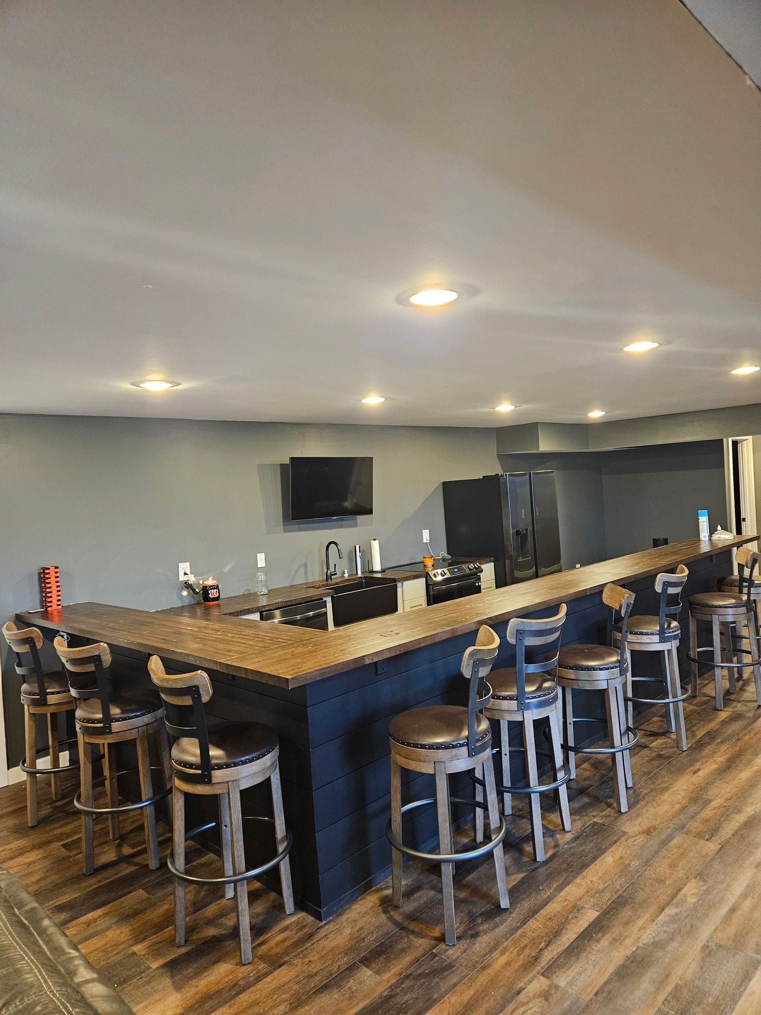 Bar with stools, dark wood counter, TV, and gray walls.
