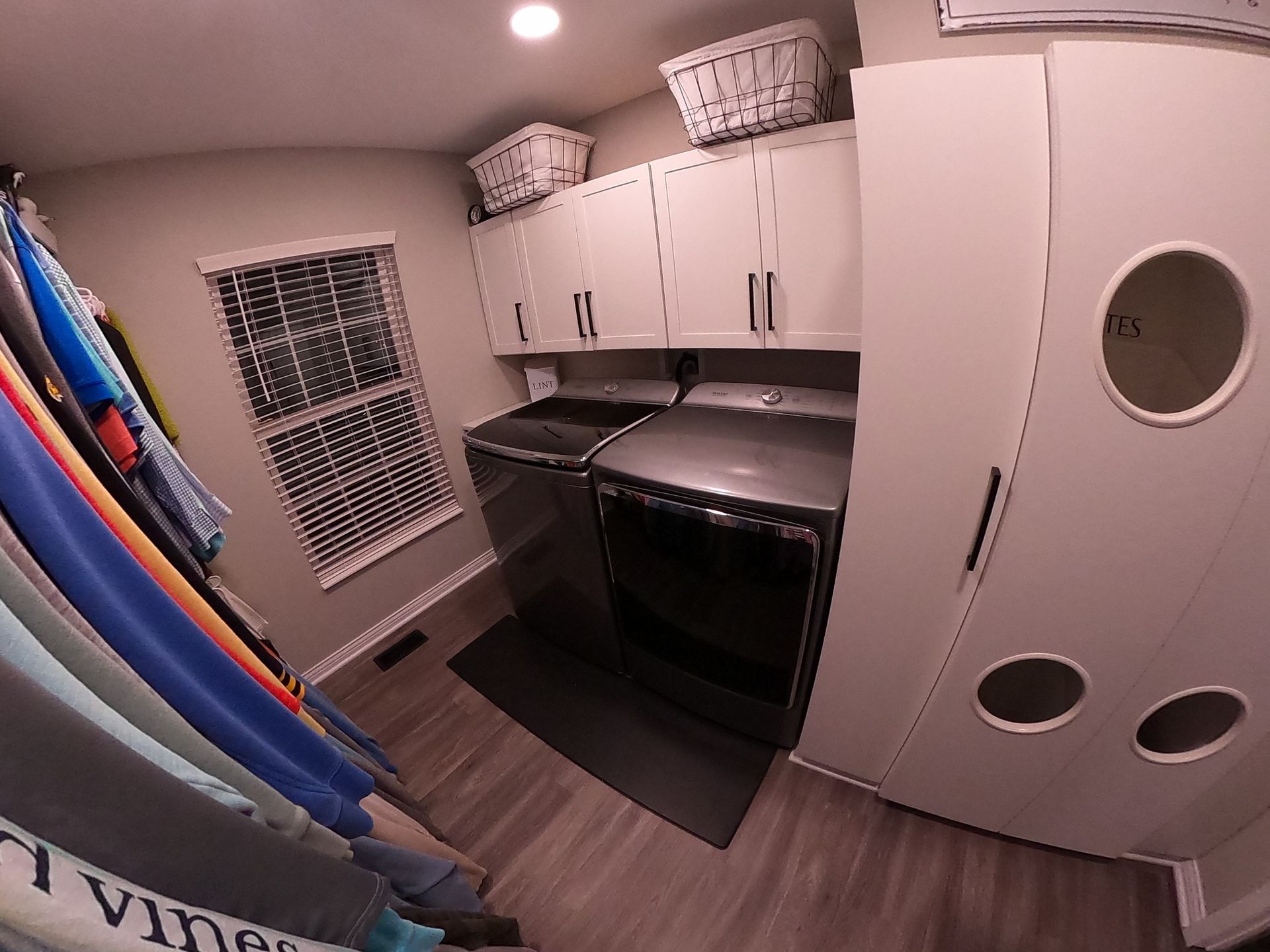 Laundry room with white cabinets, washer, dryer, window, and a door with circular cutouts.