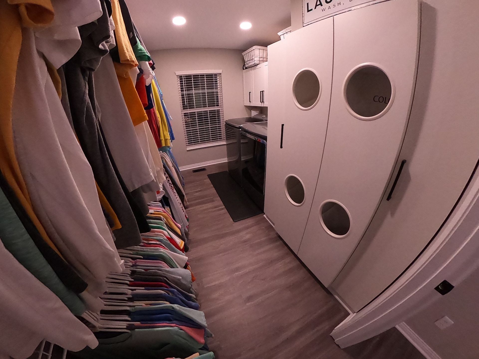 Closet with hanging clothes on left. Laundry room with storage cabinets and window.
