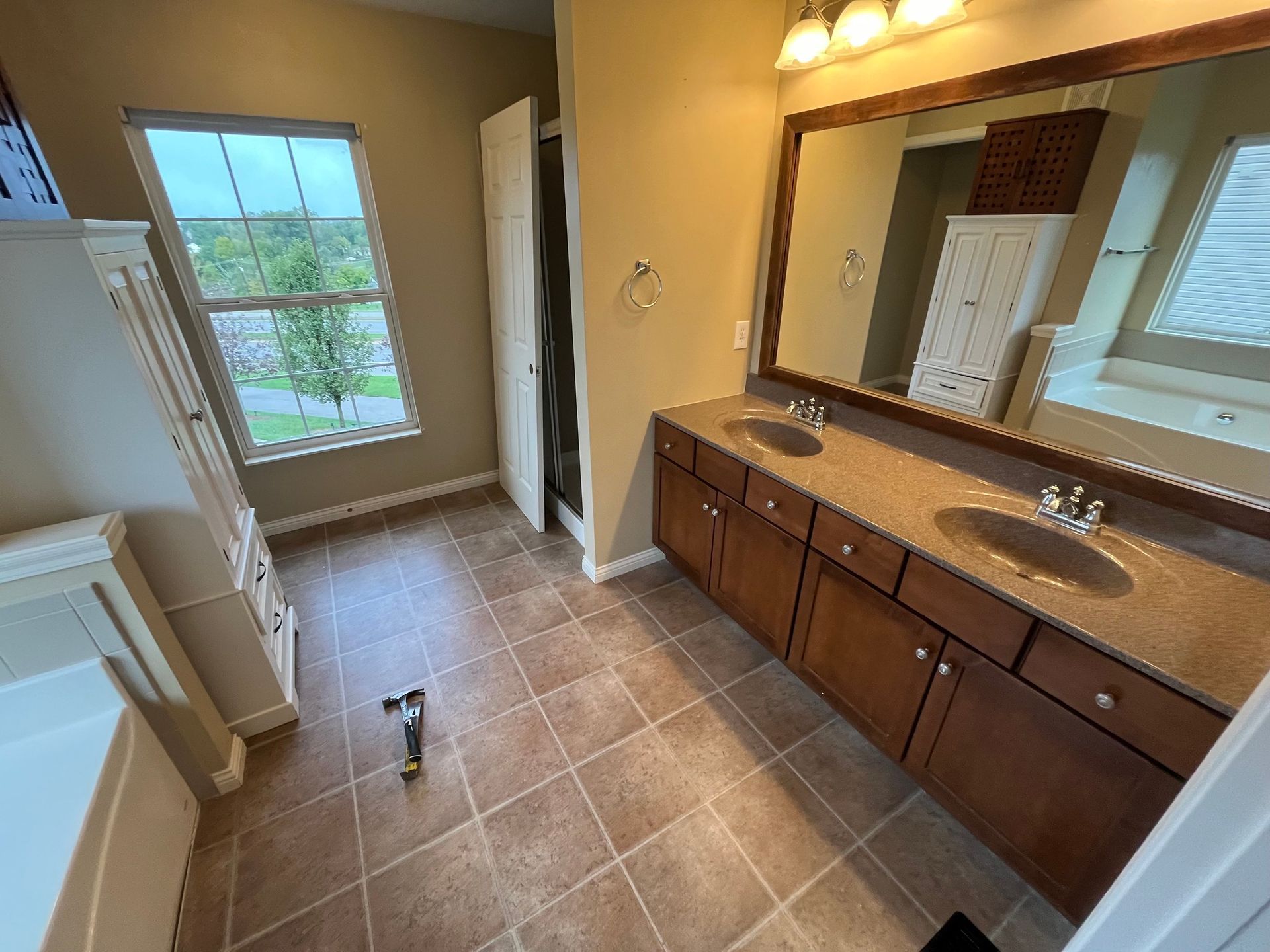 Bathroom with tile floor, double vanity, large mirror, window, and shower.