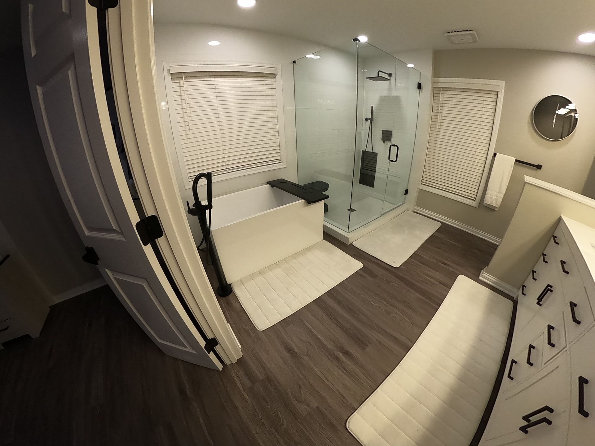 Bathroom with shower, white tub, and wood-look floors.