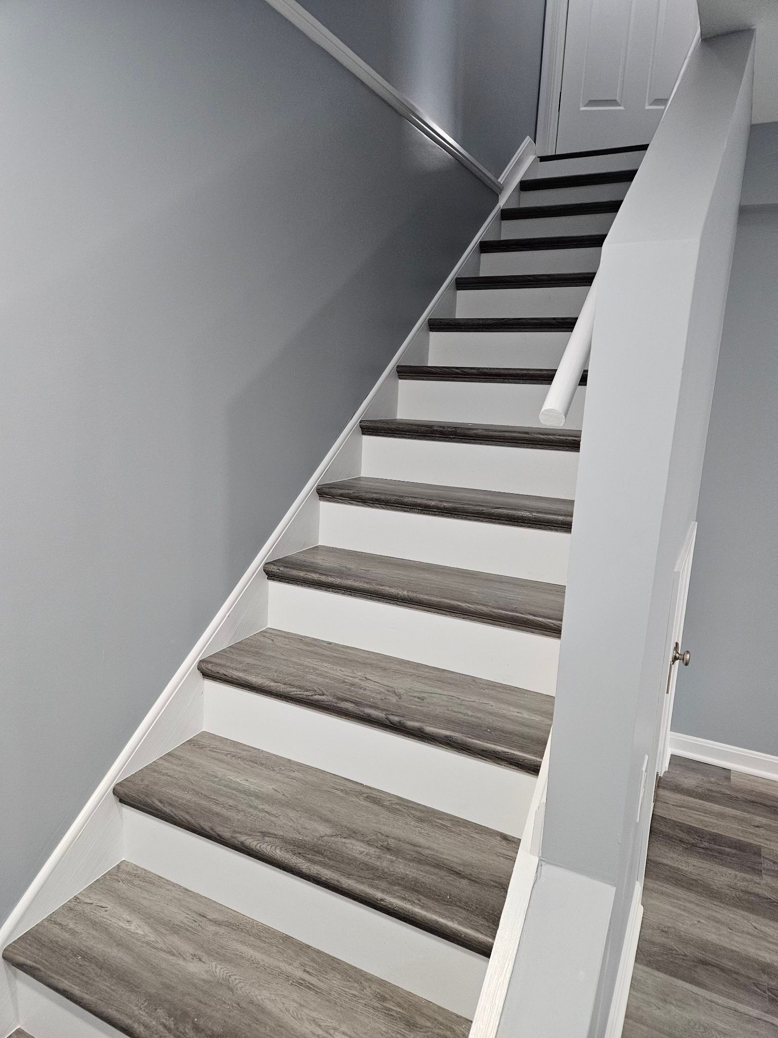 Staircase with grey wood-look steps, white risers and trim, ascending from lower right to upper left.
