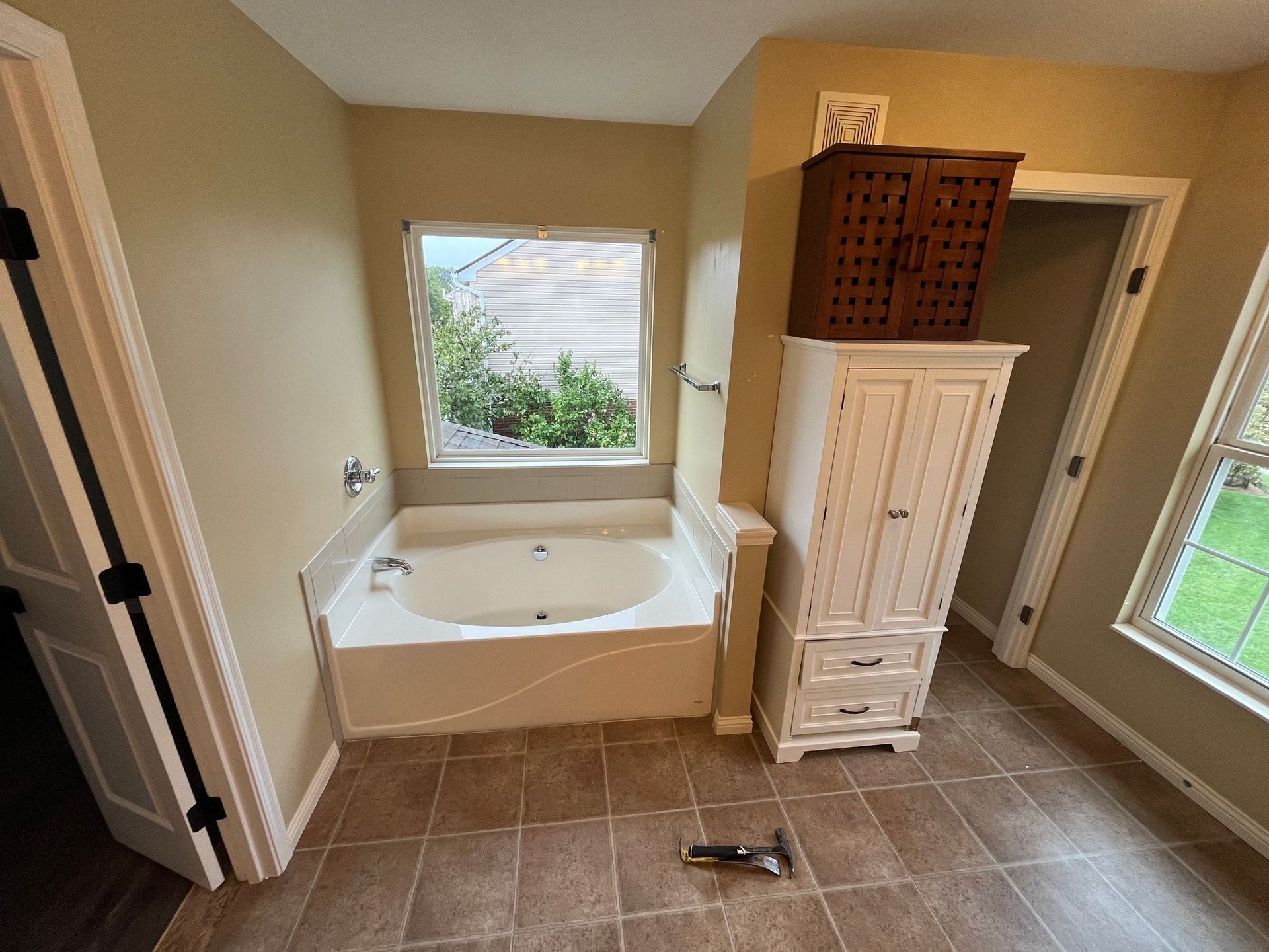Bathroom with bathtub, window, storage cabinet, and brown tile floor.