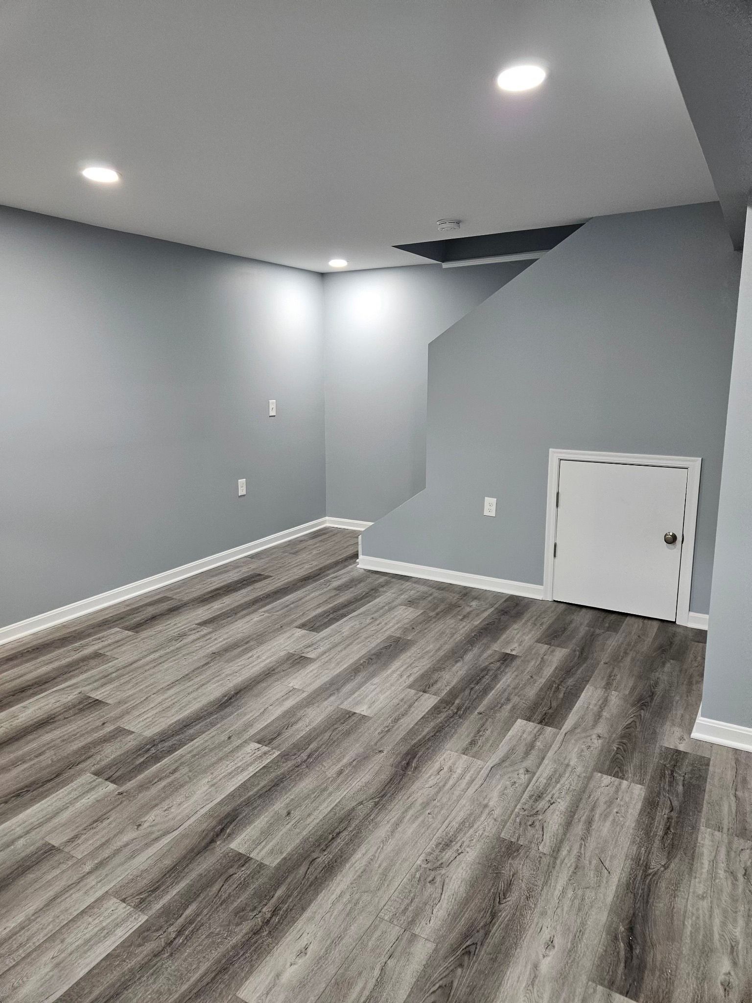 Empty room with gray walls, light wood floor, and white trim, a staircase to the ceiling.