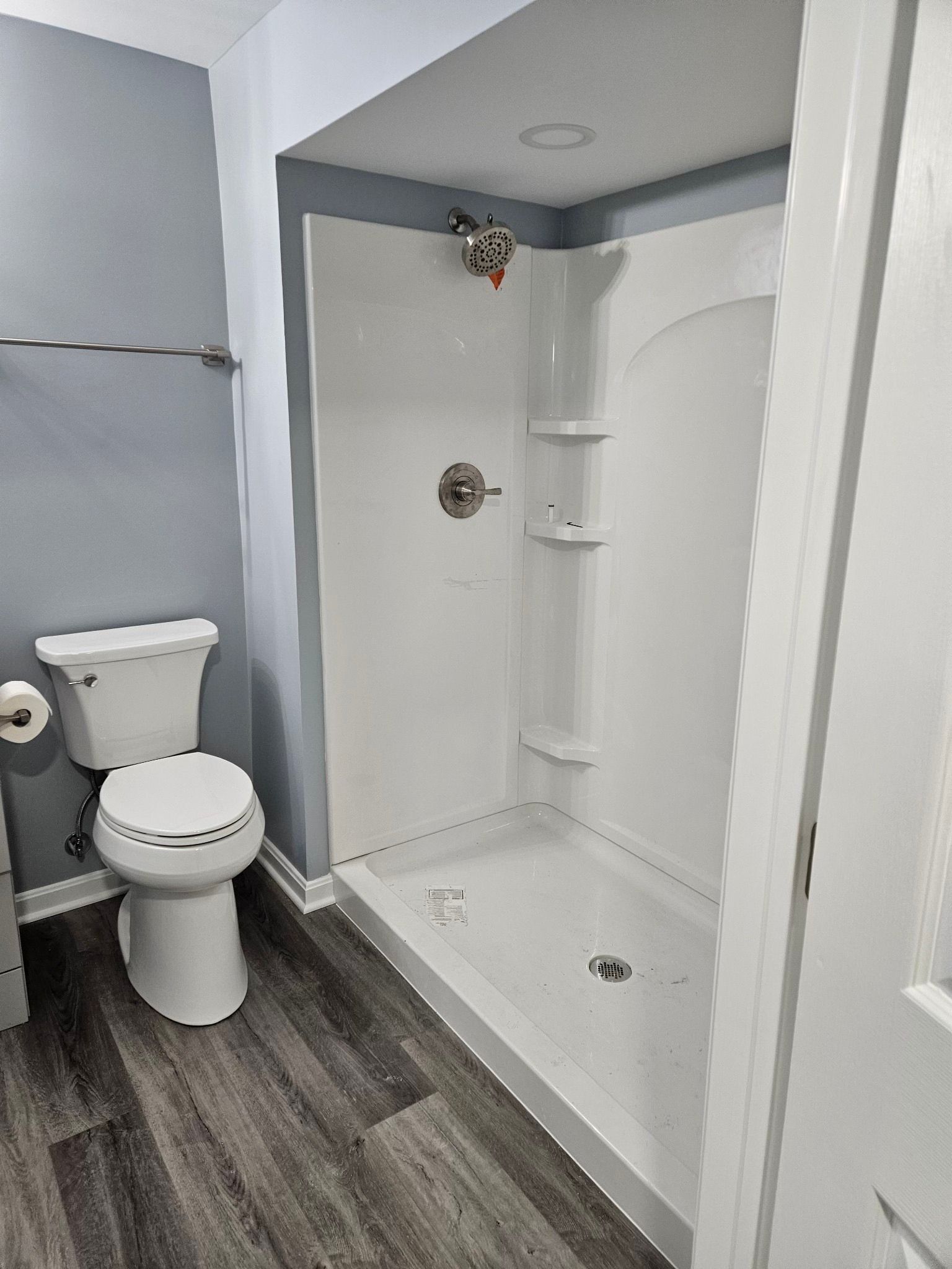 Bathroom with a white shower, gray walls, toilet, and wood-look flooring.