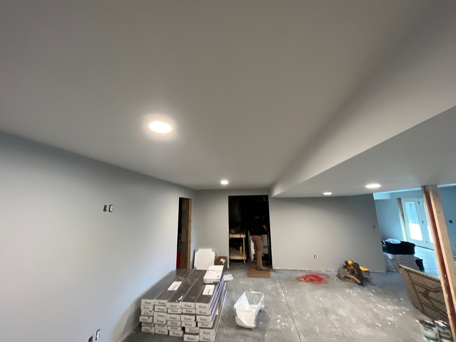 Interior room being renovated with painted walls, recessed lights, and a person standing in the doorway.