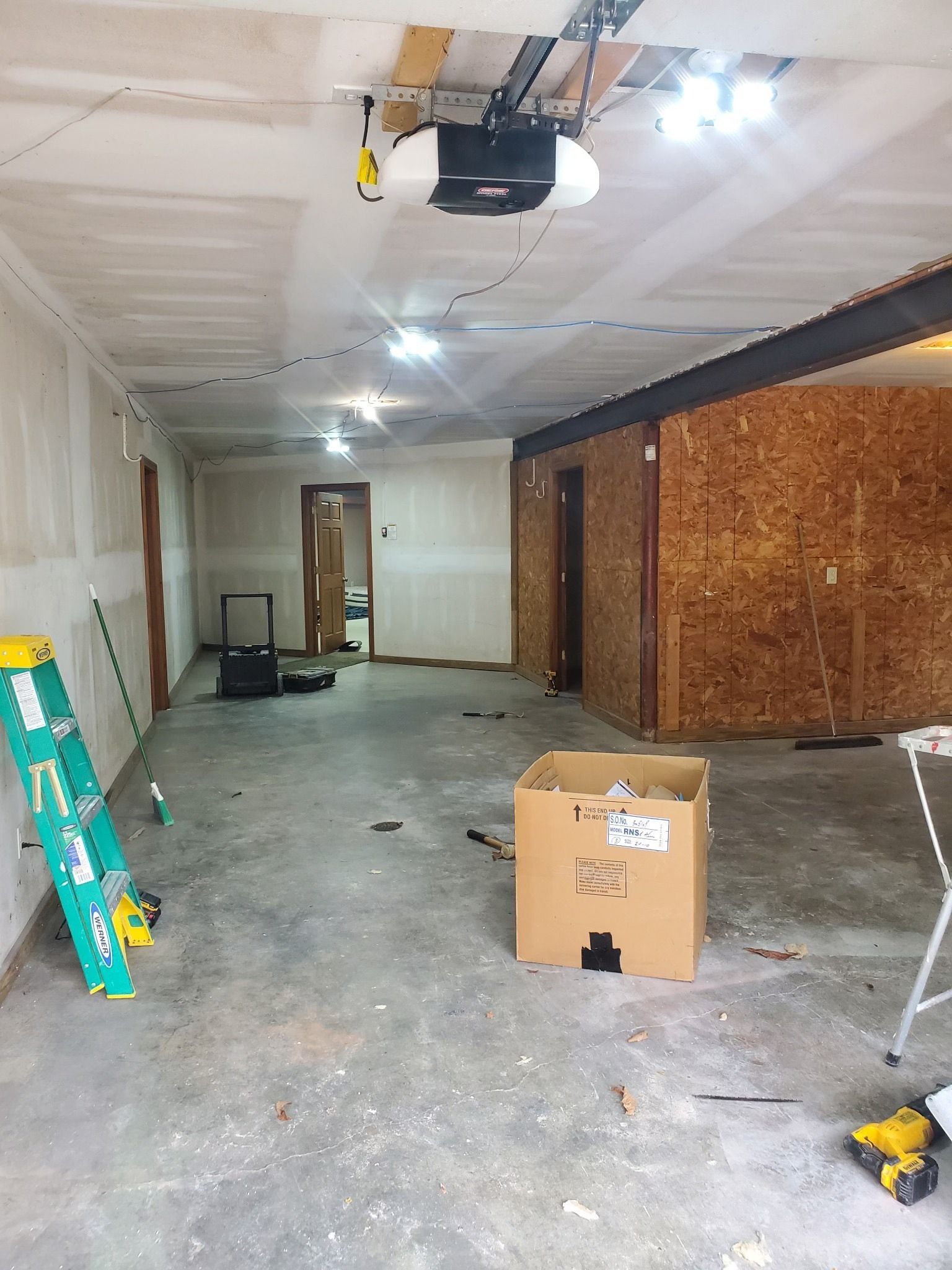 Interior of a garage under construction: concrete floor, drywall, overhead garage door, open door, boxes.