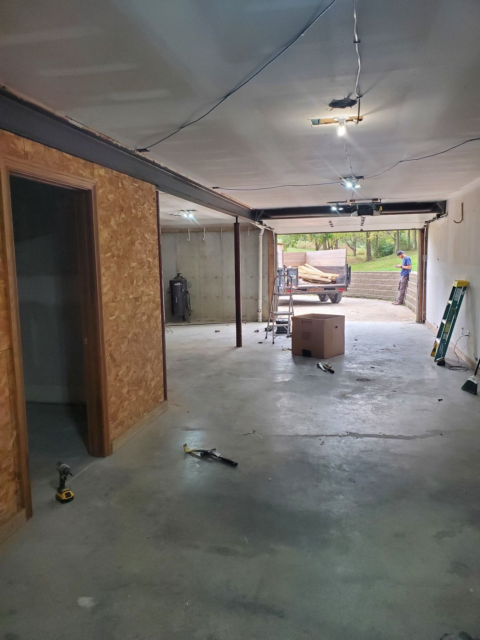 Construction of a garage interior: concrete floor, exposed ceiling, unfinished walls, and a view to the outside.