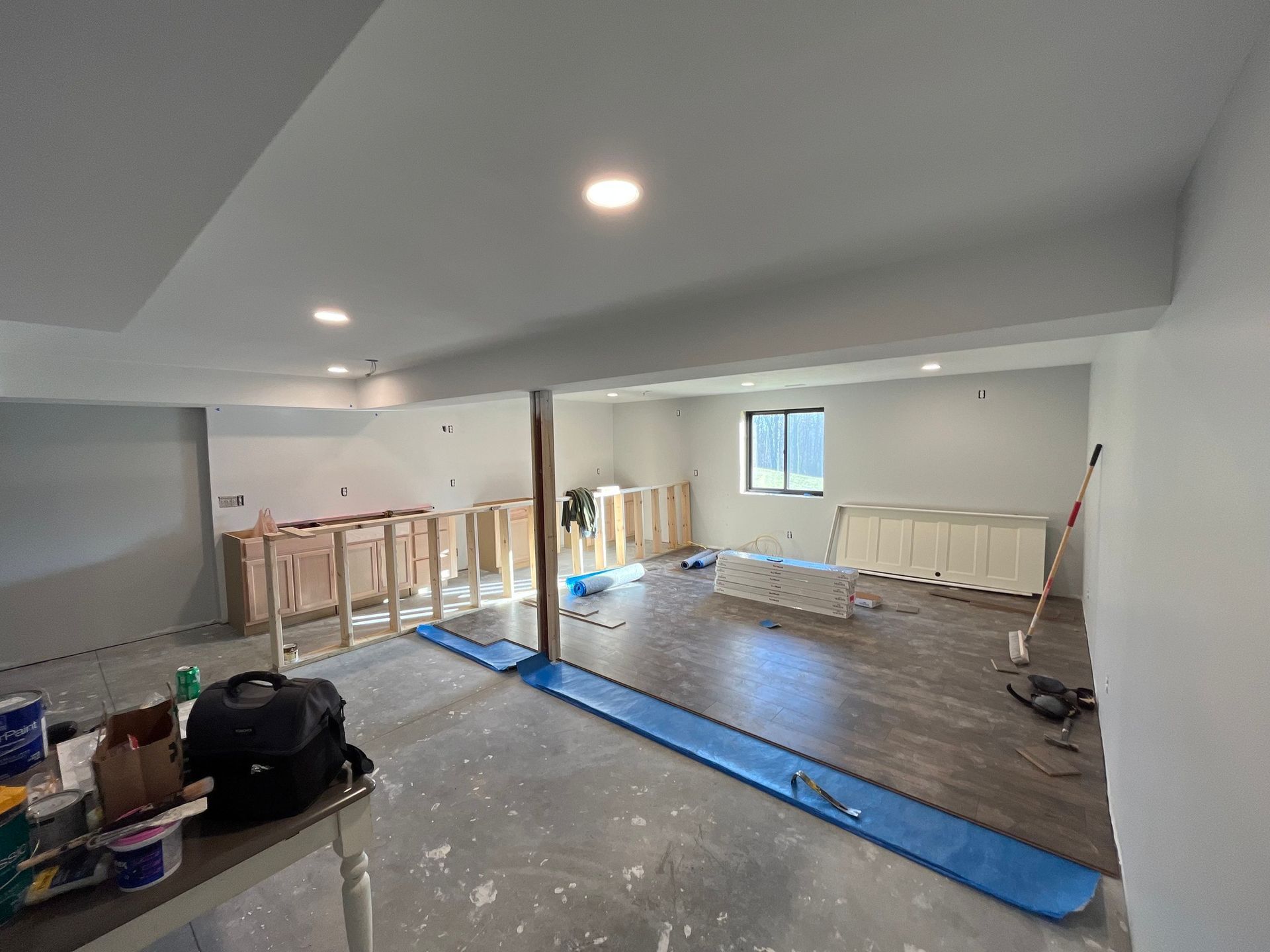 Basement renovation in progress: drywall, cabinets, and flooring being installed; tools and materials scattered.