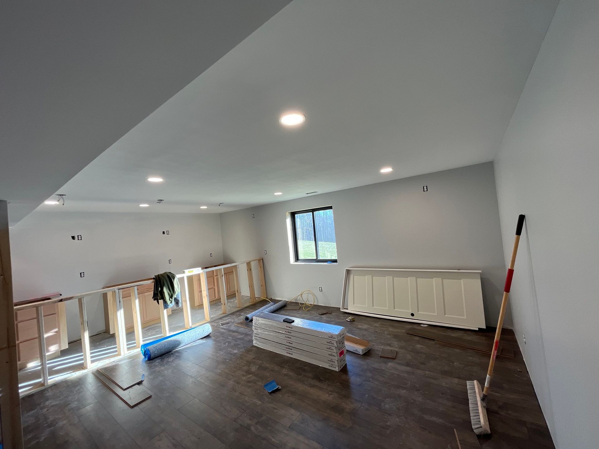 Room under construction with wooden framing, flooring, and light fixtures.