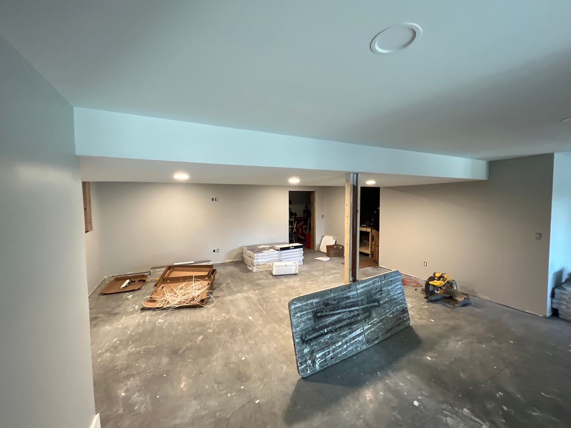 Basement interior under renovation; gray walls and floor, exposed support beam, construction materials.