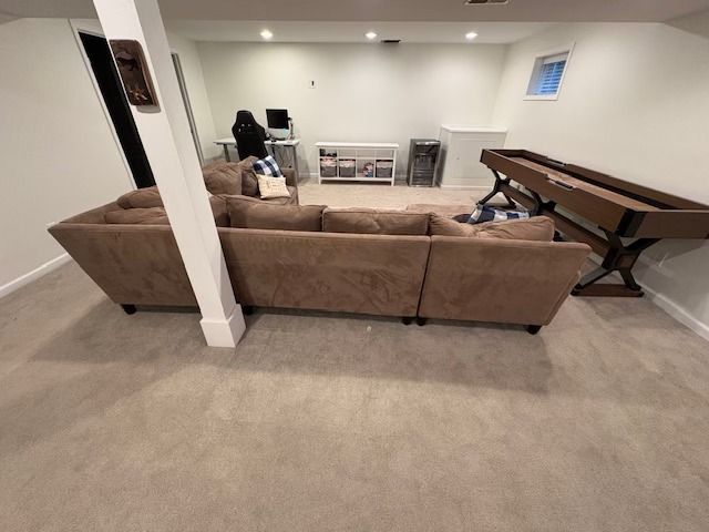 Brown sectional sofa in a finished basement with shuffleboard, desk, and light carpet.