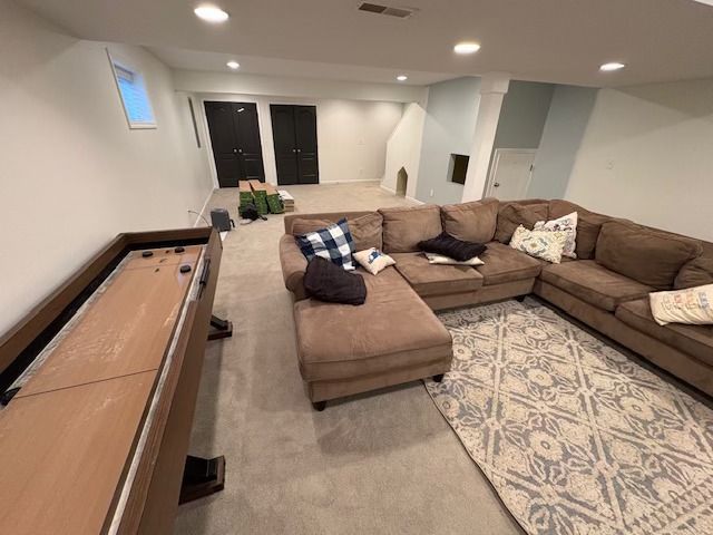 Basement living room with brown sectional sofa, shuffleboard, and patterned rug.