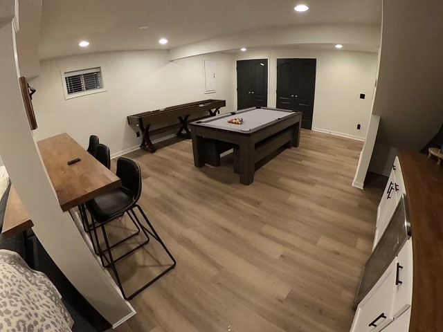 Basement game room with pool table, shuffleboard, bar, and black doors; neutral tones.