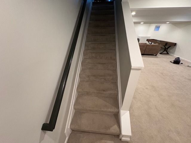 Staircase with carpeted steps, black handrail on the left, and white trim on the right leading to a finished basement.