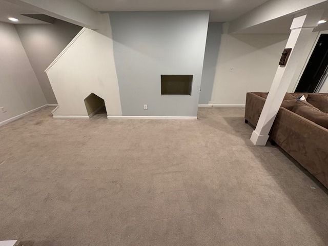 Empty finished basement with carpet, stairs, and fireplace. Blue-gray and white walls. Brown sofa.