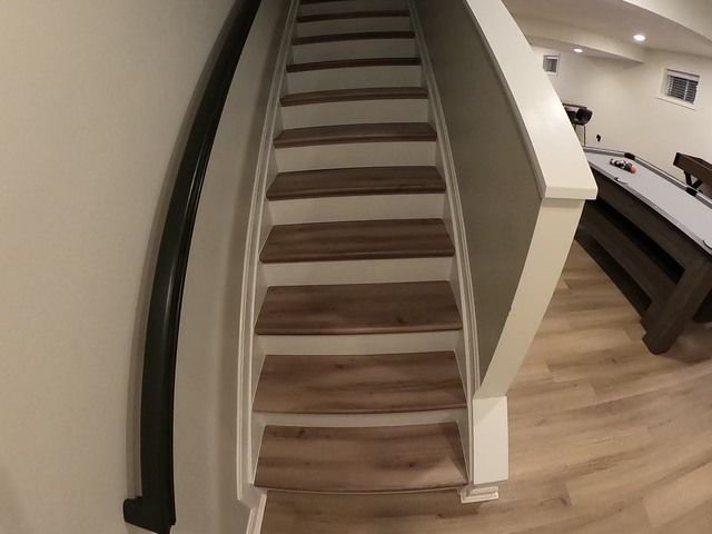 Wooden stairs leading to a basement with white trim, a dark railing, and a pool table visible.