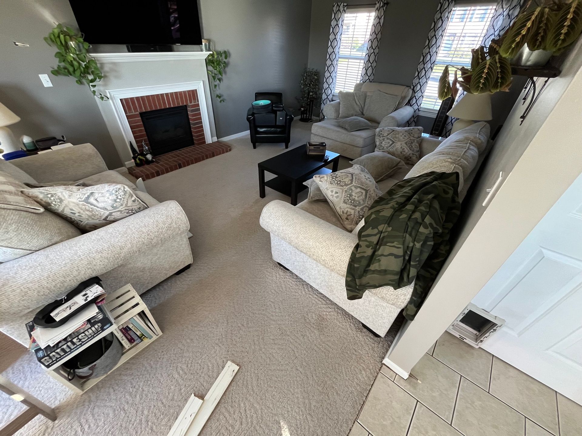 Living room with couches, fireplace, and windows. Beige carpet and light-colored furniture.