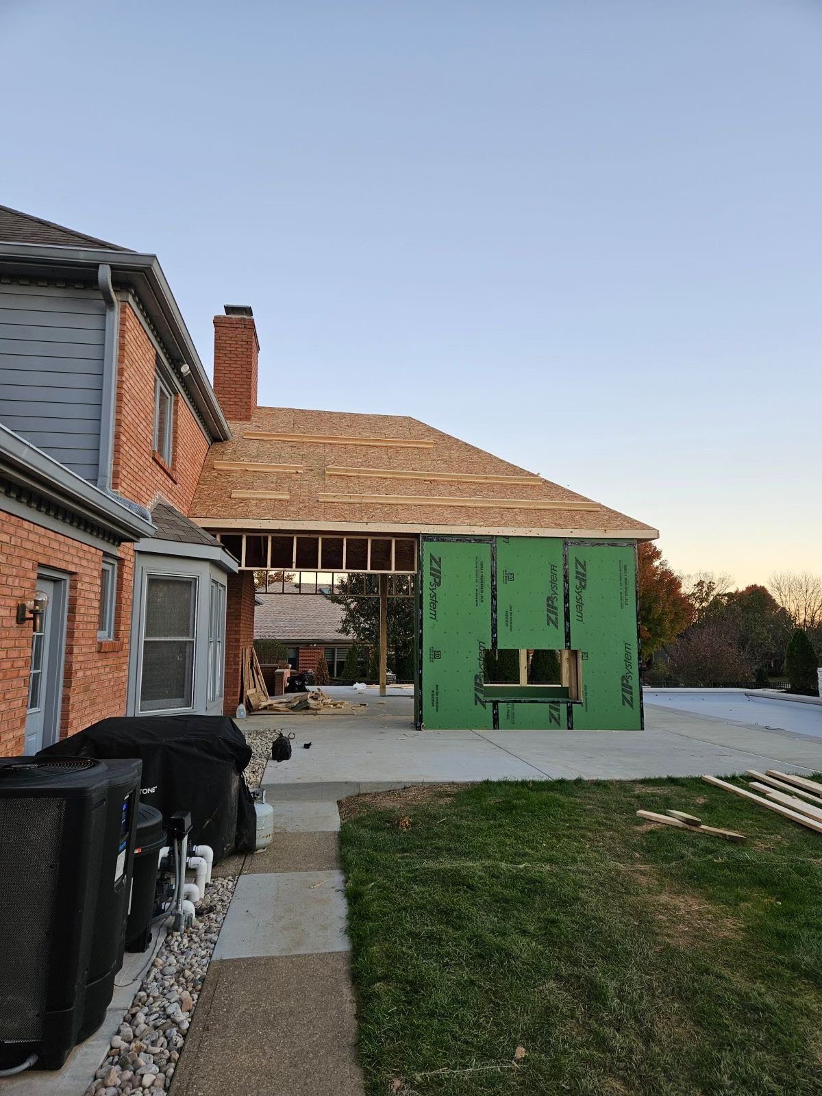House under construction with exposed framing, green sheathing, and unfinished roof.