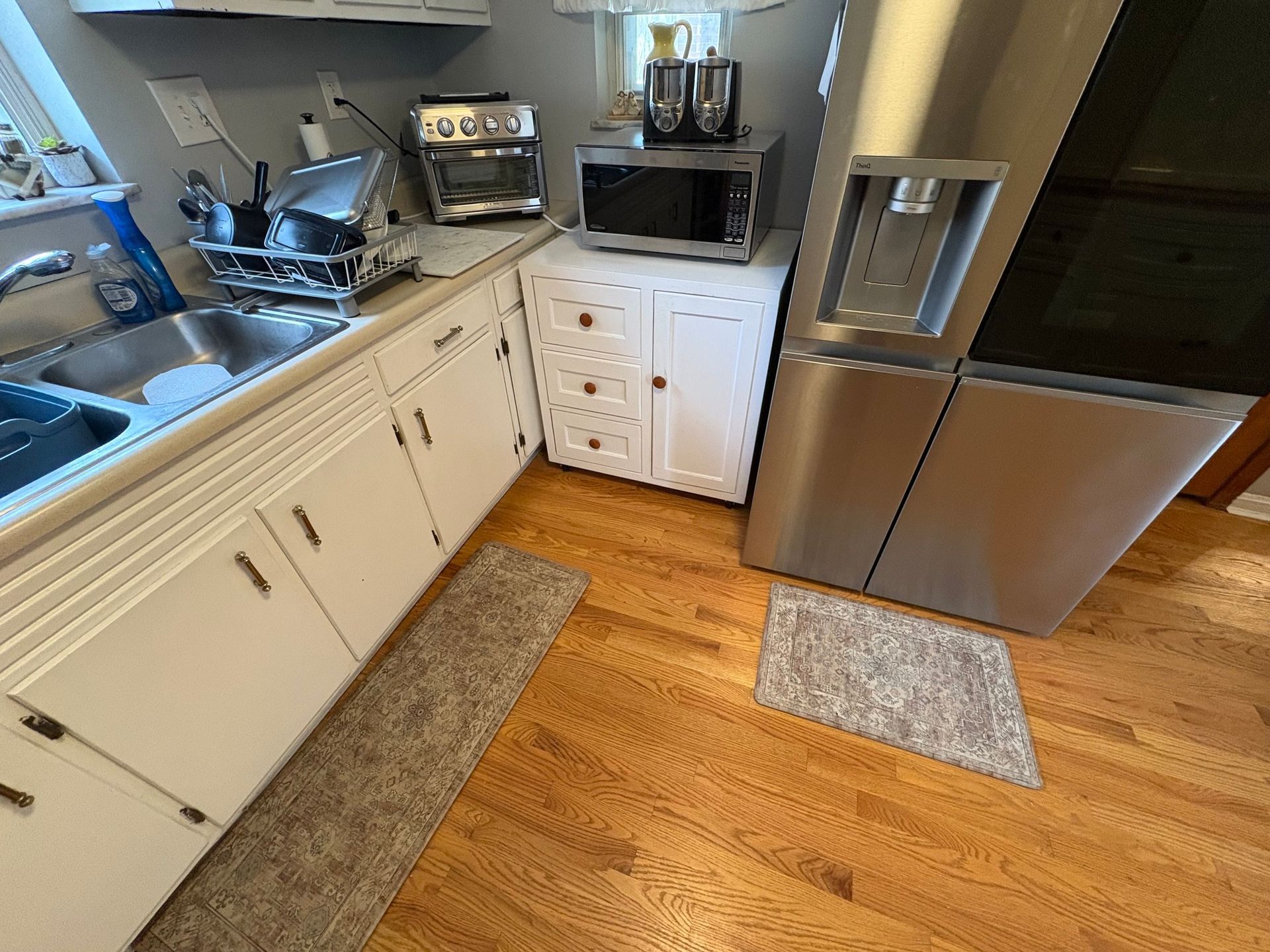 Kitchen with cabinets, sink, appliances, rug, and refrigerator on a hardwood floor.