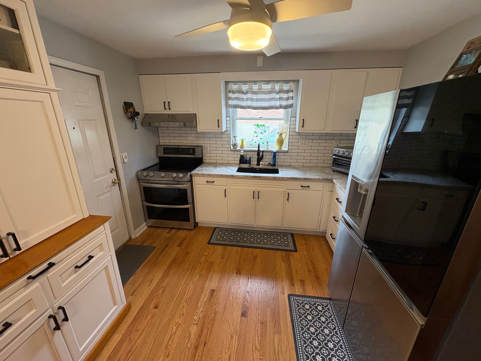 Kitchen with white cabinets, wooden floor, stainless steel appliances, and a window.