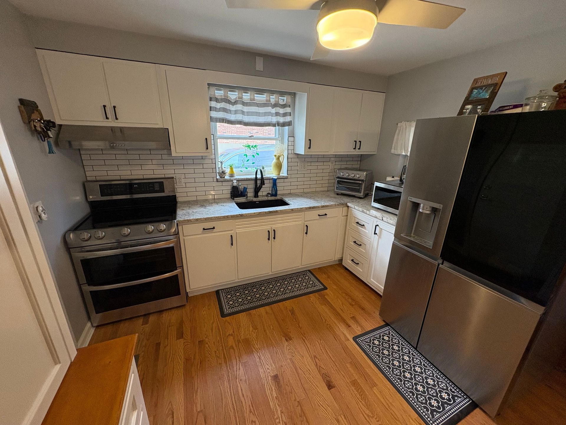 Kitchen with white cabinets, stainless steel appliances, wood floors, and a window.