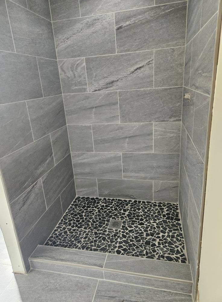 Gray tiled shower with pebble stone floor.