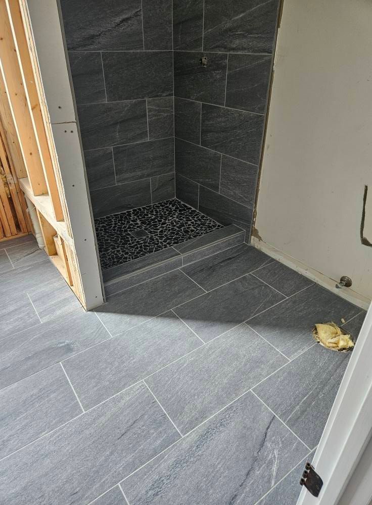 Bathroom with dark gray tiled floor and shower, and exposed wooden frame.