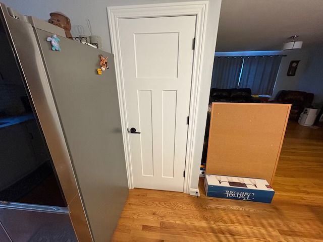 A refrigerator, white door, and a brown box are positioned on a wooden floor in a home setting.
