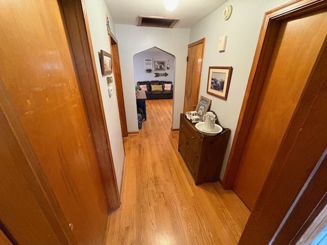 A narrow hallway with wood flooring and brown doors, leading to a living room with a couch.