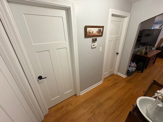 Hallway with white doors, hardwood floors, and gray walls; includes artwork and thermostat.