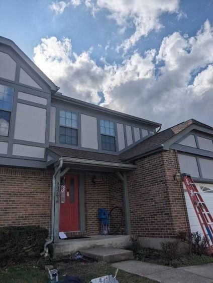 Two-story brick home with gray trim and red door; ladder propped against the side.