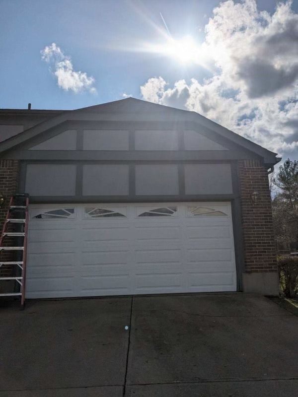 Garage with white door, brick exterior, gray trim, ladder, sunny sky.