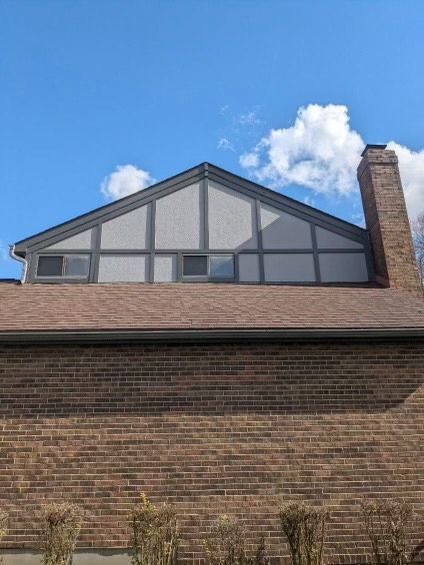 Brick building with brown roof, gray gable, and tall brick chimney against a blue sky with clouds.