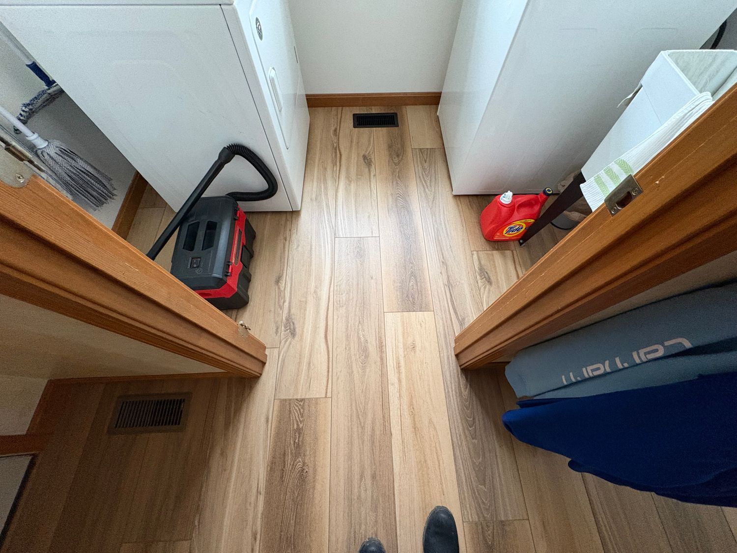 Narrow hallway with wood floors, cabinets, vacuum cleaner, and supplies.
