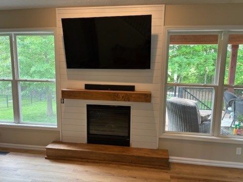 A living room with a fireplace, TV, windows, and wood accents.