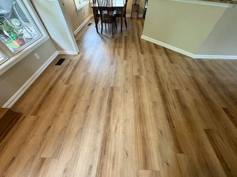Wood-look flooring in a well-lit dining room. A table and chairs sit at the end of the room.