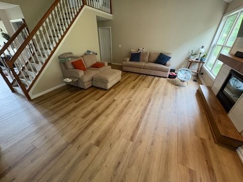 Living room with light wood flooring, beige walls, staircase, and two couches.