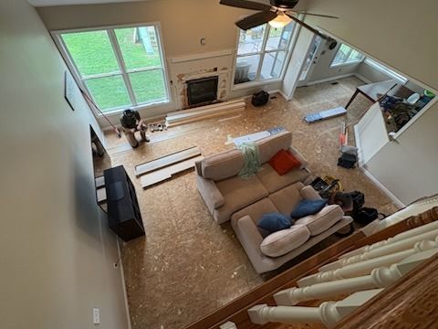 Overhead view: living room construction. A person works near a fireplace, couch on the floor, windows, and a staircase.