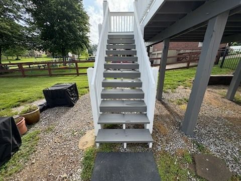 White outdoor staircase leading up to a deck, gray steps. Grassy yard and gravel below.