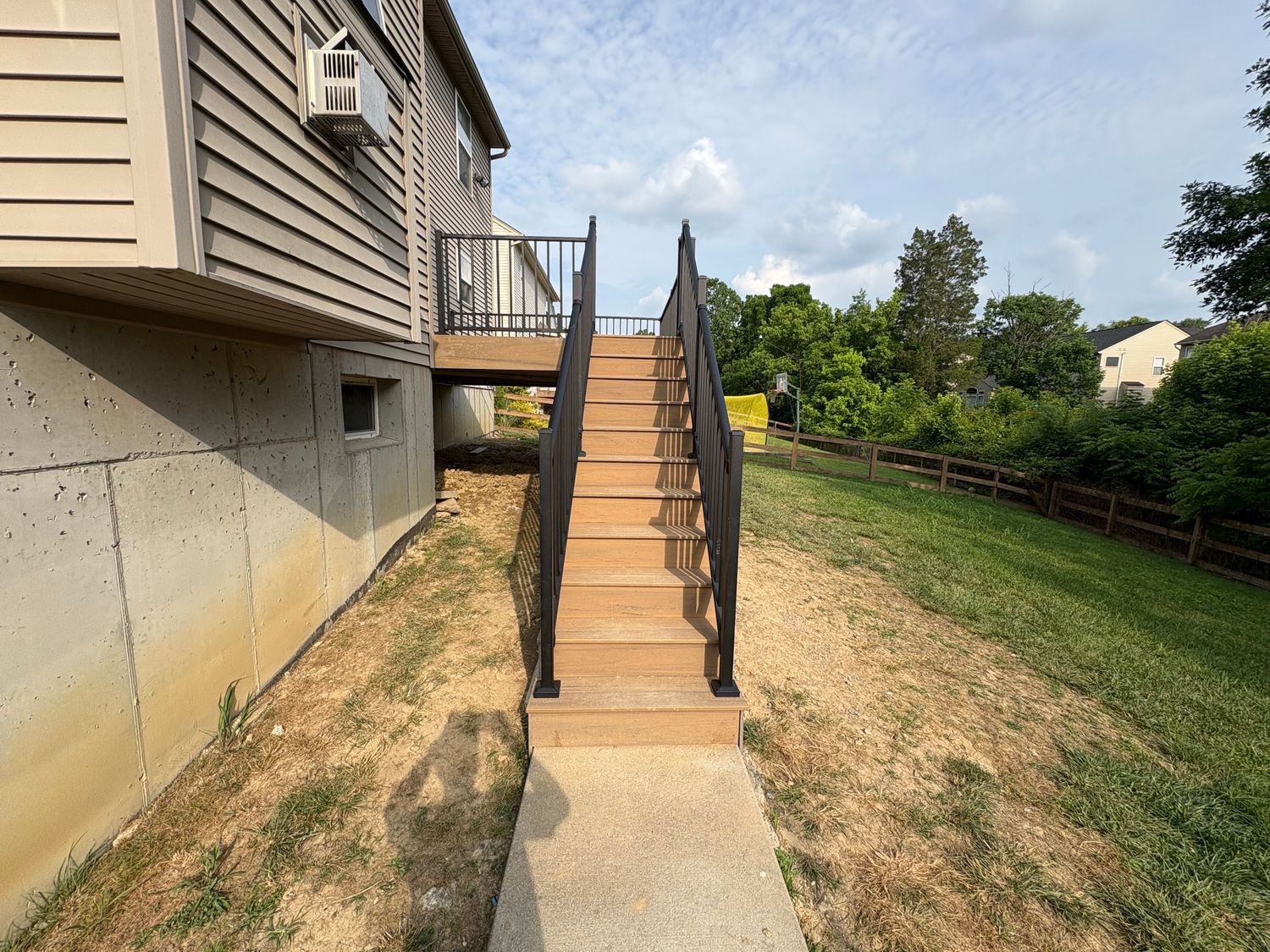 Exterior stairs leading up to a deck on a house, with black railings, built on a grassy hill.
