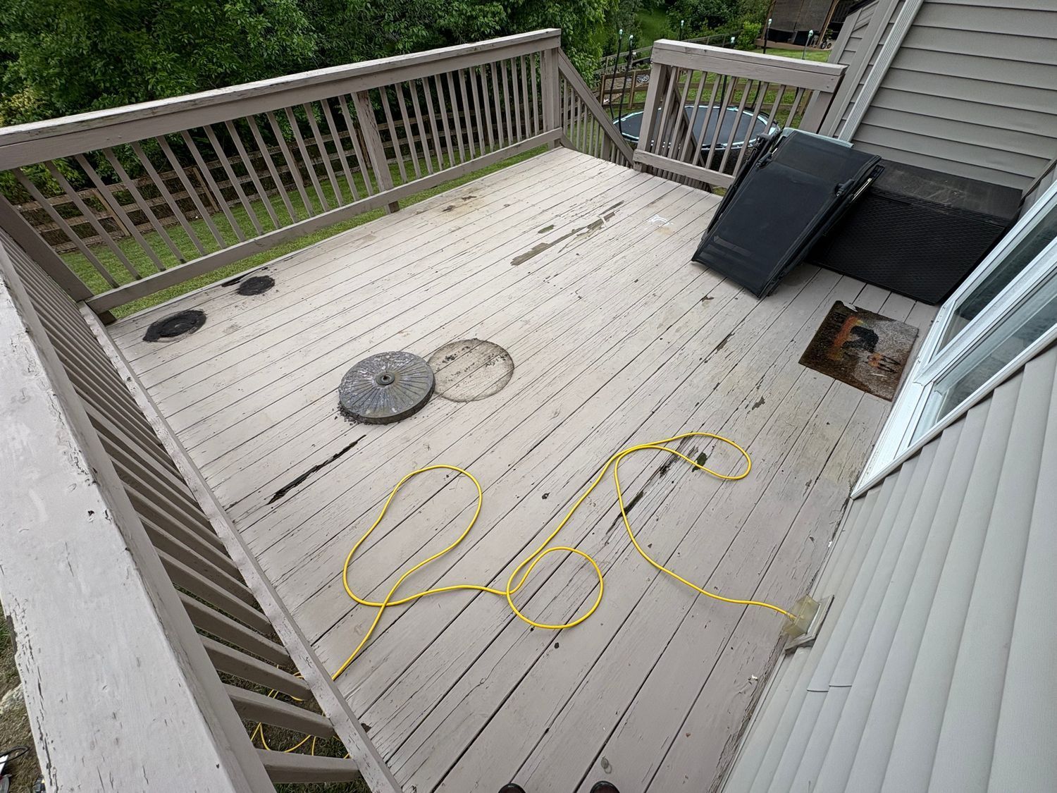 Wooden deck with railing, hose, and objects, likely outdoors, in neutral tones.