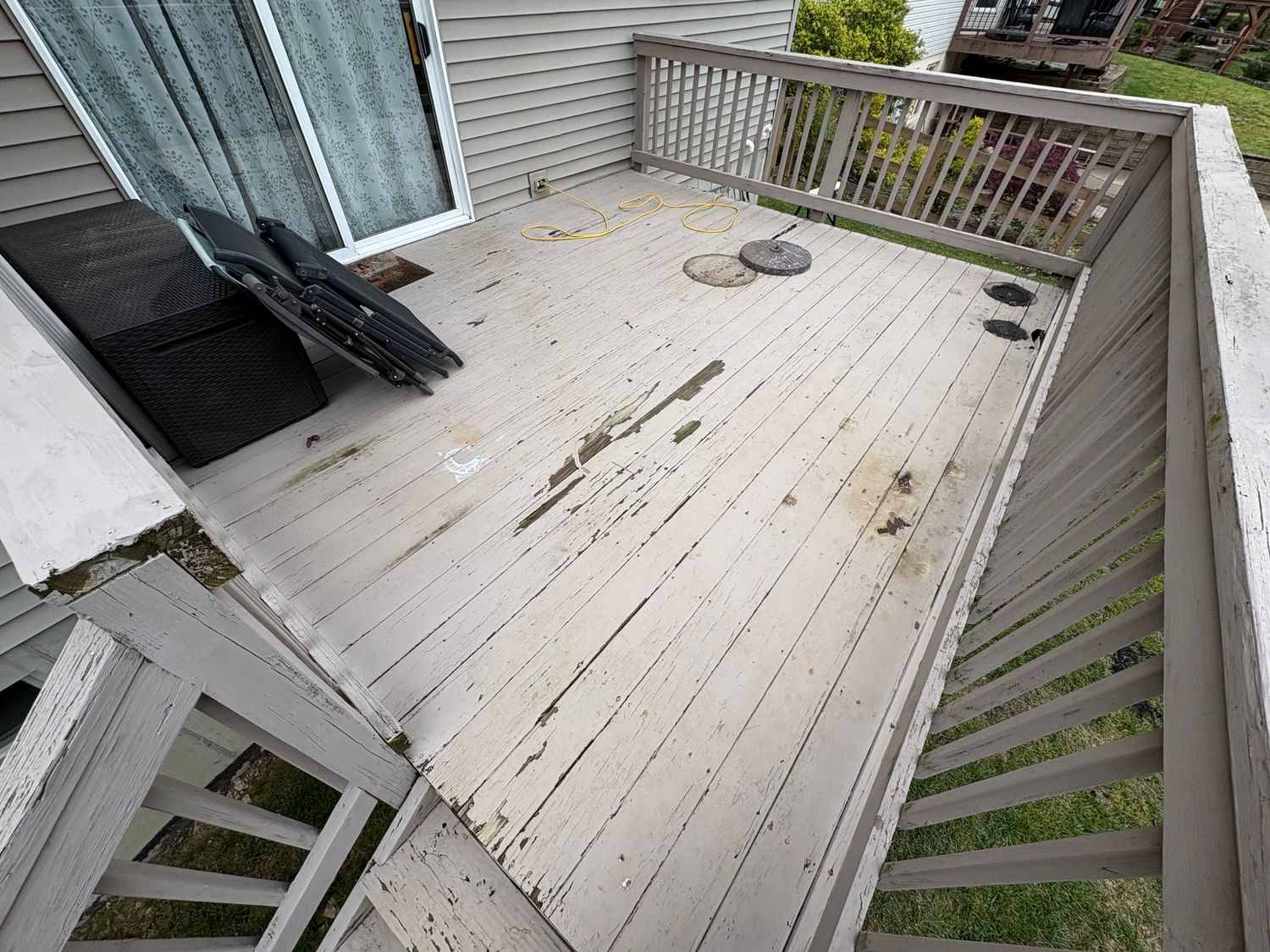 Dirty, weathered wooden deck with peeling paint; next to sliding glass doors.
