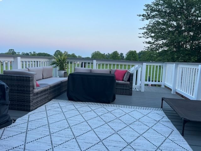 Outdoor deck with gray furniture, a white rug, and a view of a field under a dusk sky.