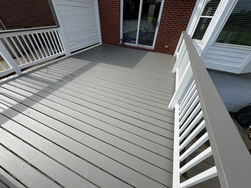 Gray deck with white railing, next to a red brick wall and a sliding glass door.